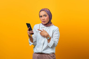 Sarı arka planda akıllı telefonu işaret eden Asyalı kadın şaşırdı.