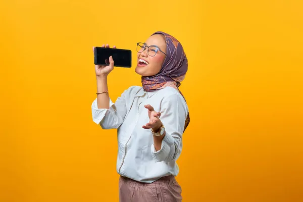 Güzel Asyalı kadın sarı arka planda akıllı telefon kullanarak şarkı söylemekten hoşlanıyor.
