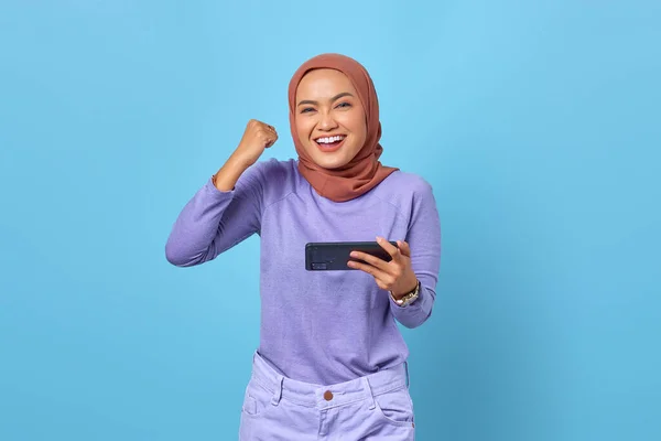 Neşeli Asyalı Kadın Mavi Arka Planda Zaferi Kutlarken Cep Telefonuyla — Stok fotoğraf