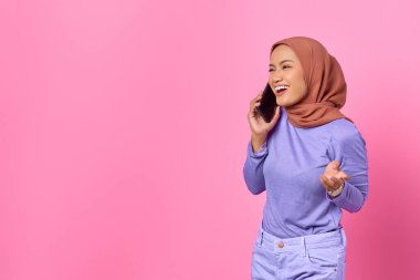 Pembe arka planda cep telefonuyla konuşan gülümseyen Asyalı genç kadının portresi.
