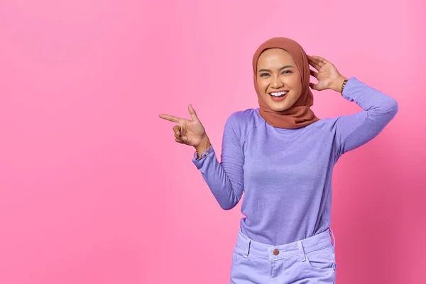 ピンクの背景にコピースペースで指を指す若いアジアの女性の笑顔の肖像 — ストック写真