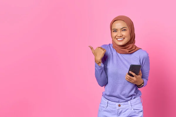 휴대폰을 분홍색 배경으로 공간을 손가락으로 가리키는 아시아 여성의 — 스톡 사진