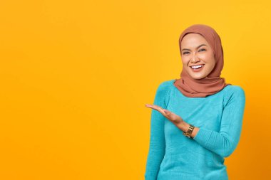 Gülümseyen Asyalı bir kadının portresi. Sarı arka planda, avuç içi izole edilmiş fotokopi alanı gösteriyor.