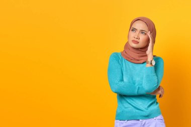 Düşünceli genç Asyalı kadın sarı arka planda bir şey düşünüyor.