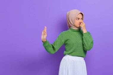 Yeşil kazaklı güzel Asyalı kadın, elini mor arka planda kapalı tutarak jest yapmayı kesiyor.