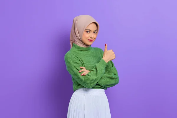 美しいです笑顔アジアの女性で緑のセーターショー親指アップジェスチャーとともに手孤立した上に紫の背景 — ストック写真