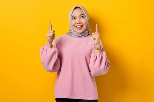 陽気若いですアジアの女性でピンクシャツPointing指アップでコピースペース上の黄色の背景 — ストック写真