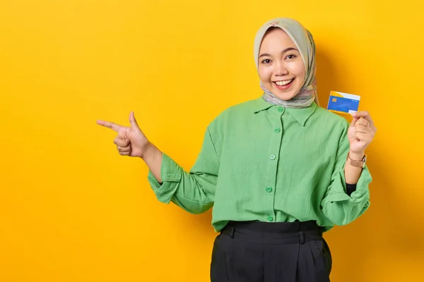 Uśmiechnięta Młoda Azjatka Zielonej Koszuli Trzymająca Kartę Kredytową Wskazująca Palcem — Zdjęcie stockowe