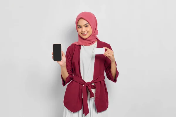 身穿休闲装 头戴头巾 展示空白手机屏幕 拿着一张白色背景的塑料信用卡的美丽的亚洲女人 人们的宗教生活方式概念 — 图库照片