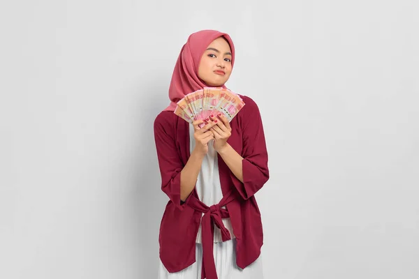 カジュアルなシャツとヒジャーブを着た美しいアジアの女性は 白い背景に孤立したインドネシアルピア紙幣を示しています 人々の宗教生活の概念 — ストック写真