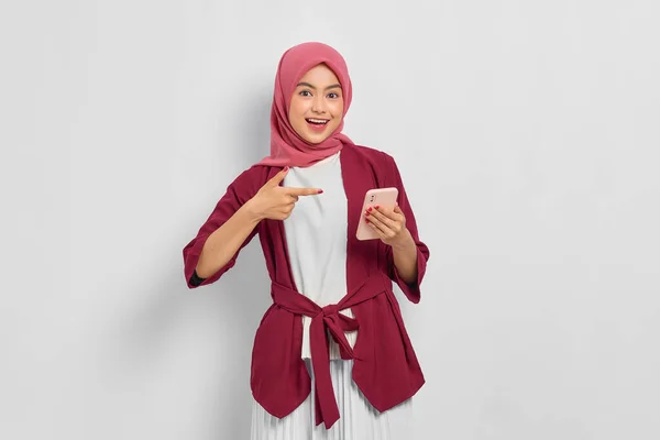 身穿休闲服 头戴头巾 手指指向白色背景的手机的快乐美丽的亚洲女人 人们的宗教生活方式概念 — 图库照片