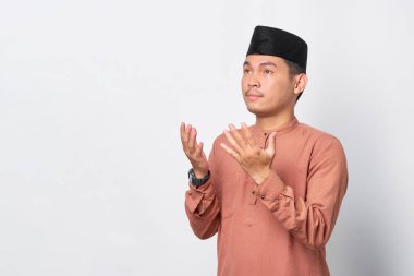Asyalı Müslüman bir adamın beyaz arka planda izole edilmiş kolları açık dua ettiği portresi.