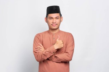 Gülümseyen Asyalı Müslüman adam beyaz arka planda izole edilmiş baş parmak hareketi gösteriyor.