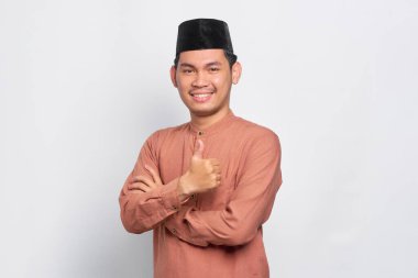 Gülümseyen Asyalı Müslüman adam beyaz arka planda izole edilmiş baş parmak hareketi gösteriyor.