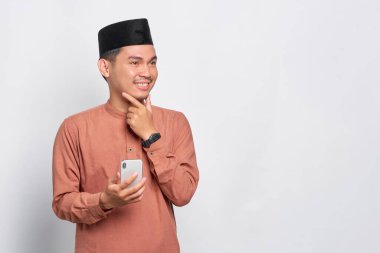 Gülümseyen Asyalı Müslüman bir adam cep telefonu kullanıyor ve beyaz arka planda izole bir şekilde yüzünü çeviriyor.