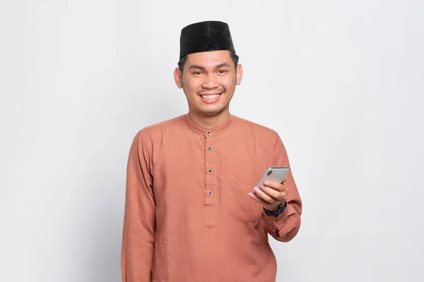 Smiling Pemuda Asia Muslim Menggunakan Ponsel Dan Melihat Kamera Terisolasi — Stok Foto