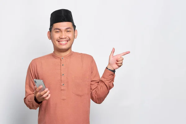 Cheerful Young Asian Muslim Man Holding Mobile Phone Pointing Finger — Stock Photo, Image