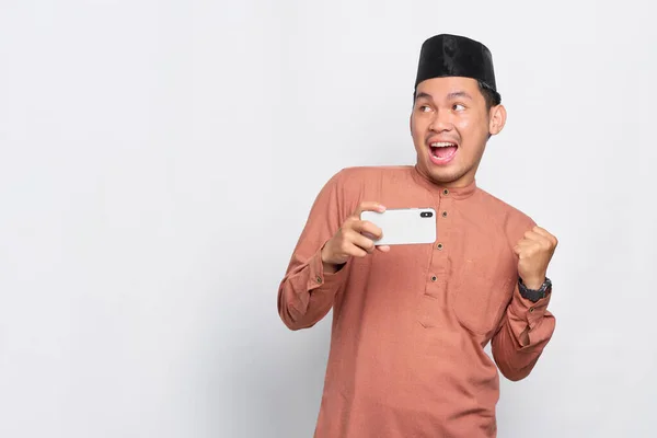 Nadšený Mladý Asijský Muslim Muž Pomocí Mobilního Telefonu Slaví Vítězství — Stock fotografie