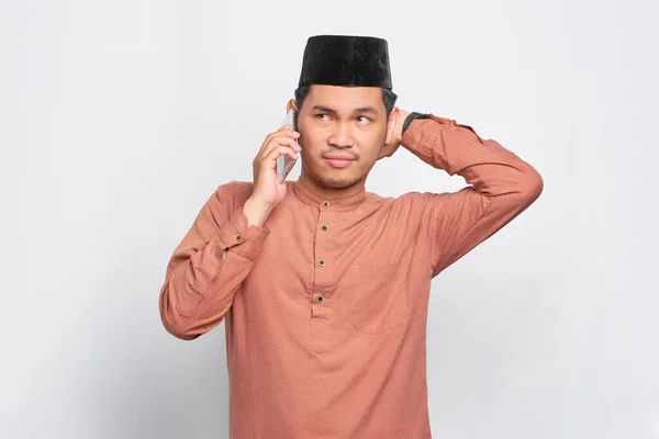 白い背景の上に隔離された携帯電話で話す若いアジア系イスラム教徒の男を混乱させ — ストック写真