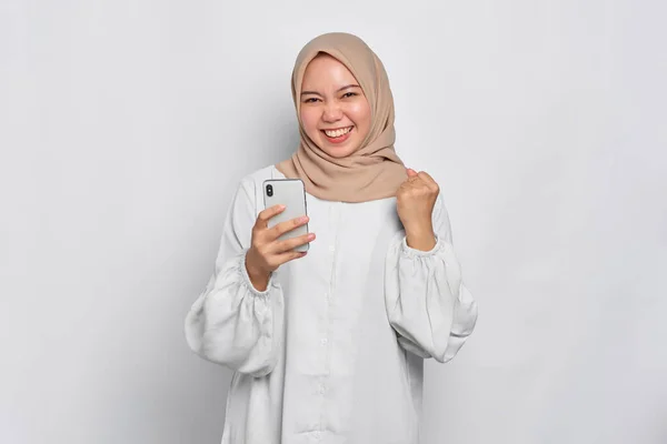 Возбужденная Молодая Азиатская Мусульманка Пользующаяся Мобильным Телефоном Празднующая Успех Получает — стоковое фото