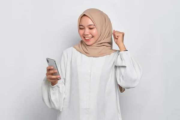 携帯電話を使用して興奮した若いアジアのイスラム教徒の女性と成功を祝う 白い背景に隔離された良いニュースを取得 — ストック写真