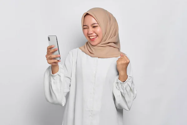 兴奋的年轻的亚洲穆斯林妇女使用手机庆祝成功 得到了好消息与白人背景隔离 — 图库照片