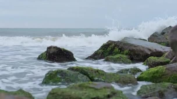 Bulutlu bir havada deniz manzarası ve kaya parçalarına çarpan dalgalar. — Stok video