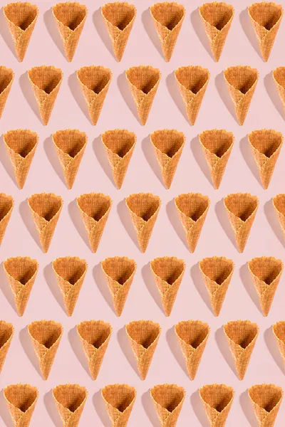 ピンクの背景にパターンで配置されたアイスクリームのためのシュガーワッフルコーン。コピースペース付きのイメージは、お菓子メニューのデザインの背景として使用できます。 — ストック写真
