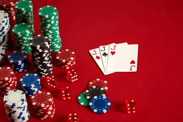 Игровое покерное оборудование казино и развлекательная концепция - крупным планом игры в карты и фишки на красном фоне. Трое из одного — стоковое фото