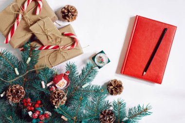 Noel ya da Yeni Yıl arkaplanı: kürk ağacı, dallar, hediyeler, dekorasyon, beyaz arkaplanlı kırmızı defter