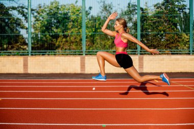 Yan görünümü güzel genç kadın egzersiz koşu ve atletik yolda stadyum üzerinde çalışan