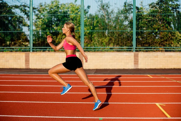 Oldalnézet gyönyörű fiatal nő gyakorlása kocogás és a futás a atlétikai pálya, a stadion — Stock Fotó