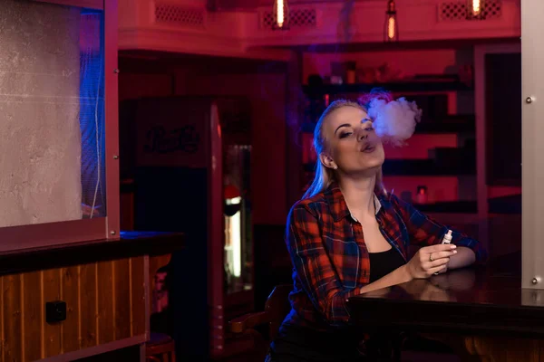 Młoda piękna kobieta w koszuli w klatce pali elektronicznego papierosa w vape barze — Zdjęcie stockowe