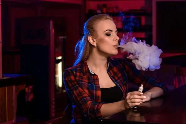 Young pretty woman in a shirt in a cage smoke an electronic cigarette at the vape bar — Stock Photo, Image