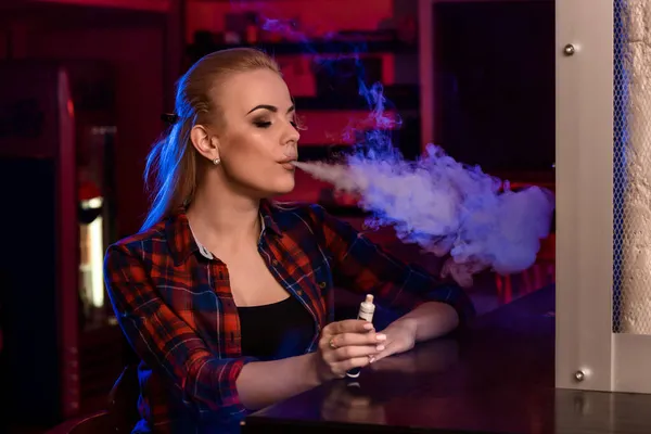 Młoda piękna kobieta w koszuli w klatce pali elektronicznego papierosa w vape barze — Zdjęcie stockowe