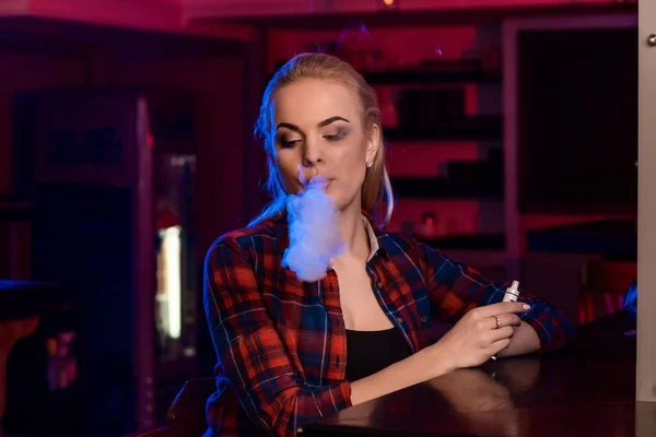 Jovem mulher bonita em uma camisa em uma gaiola fumam um cigarro eletrônico no bar vape — Fotografia de Stock