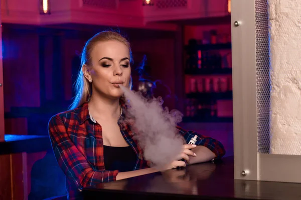 Kafesteki tişörtlü güzel bir kadın Vape Bar 'da elektronik sigara içiyor. — Stok fotoğraf