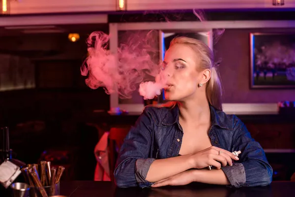 Young pretty woman smoke an electronic cigarette at the vape bar — Stock Photo, Image