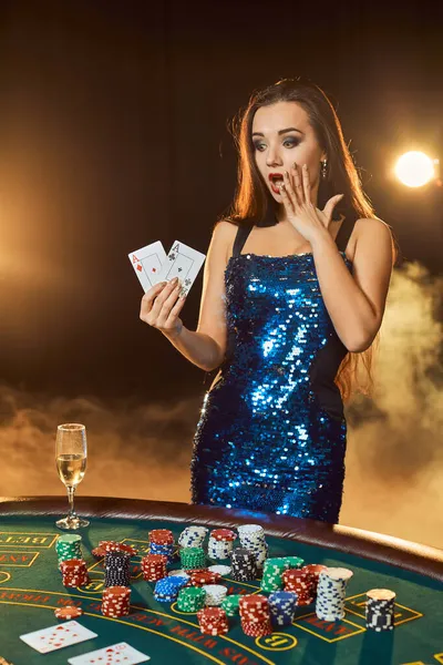 Giovane bella donna posa vicino tavolo da poker nel casinò di lusso. La passione, le carte, le patatine fritte, l'alcool, i dadi, il gioco d'azzardo, il casino - è come divertimento femminile. Sfondo fumo. — Foto Stock