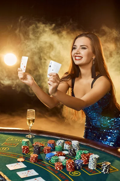 Ung vacker kvinna poserar nära pokerbordet i lyx casino. Passion, kort, chips, alkohol, tärningar, spel, kasino - det är som kvinnlig underhållning. Rökbakgrund. — Stockfoto