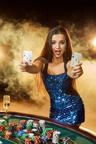 若い美しい女性は豪華なカジノのポーカーテーブルの近くにポーズします。情熱、カード、チップ、アルコール、ダイス、ギャンブル、カジノ-それは女性のエンターテイメントとしてです。煙の背景. — ストック写真