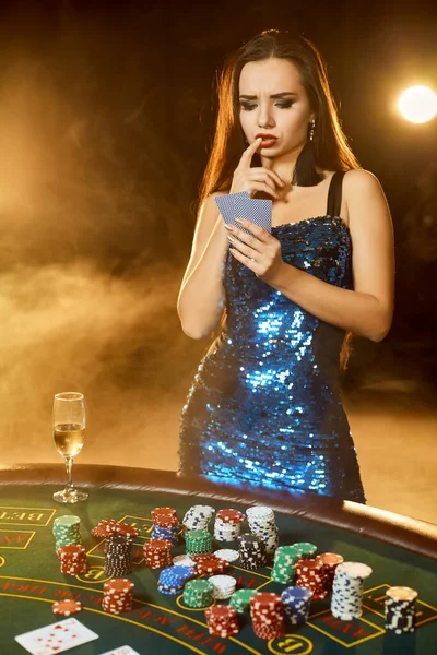 Junge schöne Frau posiert am Pokertisch im Luxus-Casino. Leidenschaft, Karten, Chips, Alkohol, Würfel, Glücksspiel, Casino - es ist weibliche Unterhaltung. Hintergrund der Rauchentwicklung. — Stockfoto