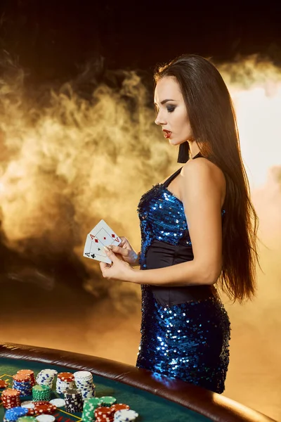 Νεαρή όμορφη γυναίκα θέτει κοντά στο τραπέζι πόκερ στο πολυτελές καζίνο. Πάθος, κάρτες, μάρκες, αλκοόλ, ζάρια, τυχερά παιχνίδια, καζίνο - είναι ως γυναικεία ψυχαγωγία. Καπνός. — Φωτογραφία Αρχείου