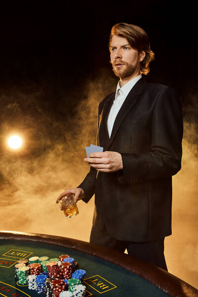 A man in a business suit standing near the game table. Male player. Passion, cards, chips, alcohol, dice, gambling, casino - it is as male entertainment.