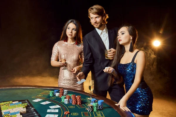 Twee mooie vrouwen en jonge man spelen op pokertafel in casino, focus op man en brunette — Stockfoto