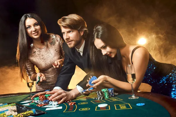 Dos hermosas mujeres y un hombre joven juegan en la mesa de póquer en el casino, se centran en el hombre y la morena — Foto de Stock