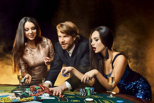 Duas mulheres bonitas e jovem jogam na mesa de poker no cassino, se concentram no homem e na morena — Fotografia de Stock