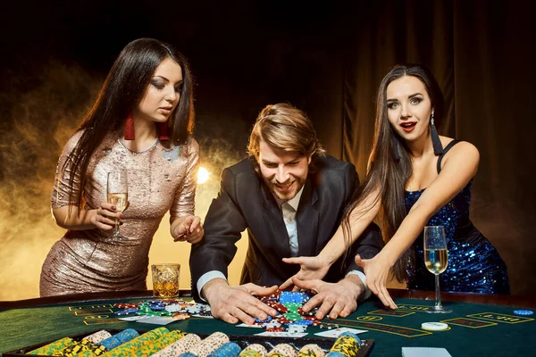 Zwei schöne Frauen und ein junger Mann spielen am Pokertisch im Casino, konzentrieren sich auf Mann und Brünette — Stockfoto