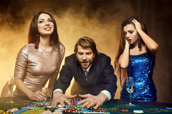 二つの美しい女性と若い男はカジノのポーカーテーブルで遊ぶ,男とブルネットに焦点を当てる — ストック写真