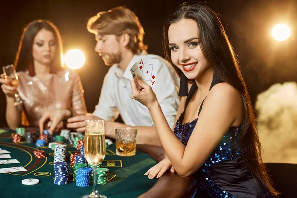 Group of an elegant people playing poker at the gambling house. Focus on a luxurious brunette in a blue shiny dress — Stock Photo, Image